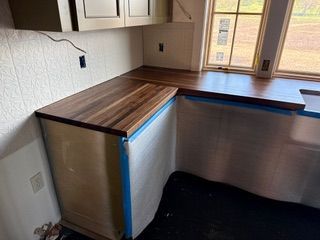 Empty kitchen corner with dark wood counters and stainless-steel cabinet fronts, by a window.