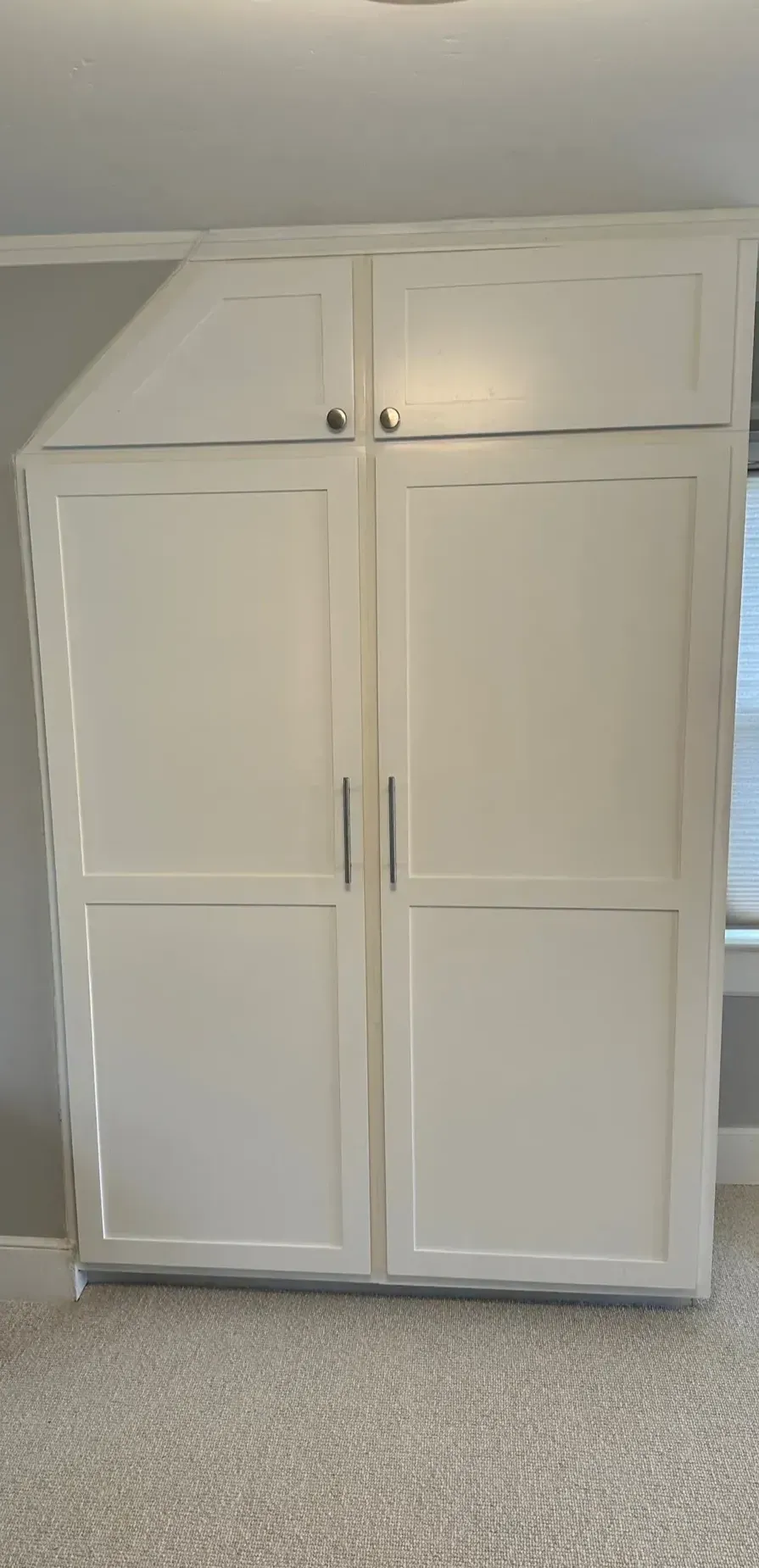 A large white cabinet is sitting in a room next to a window.