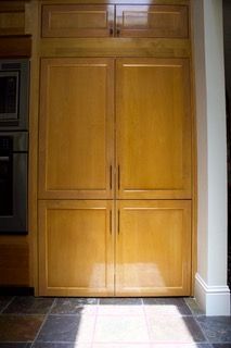 Wooden kitchen cabinet with four doors and drawers, set against a white wall and tiled floor.