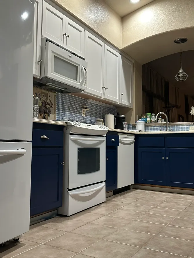 A kitchen with blue cabinets , white appliances , a refrigerator and a microwave.