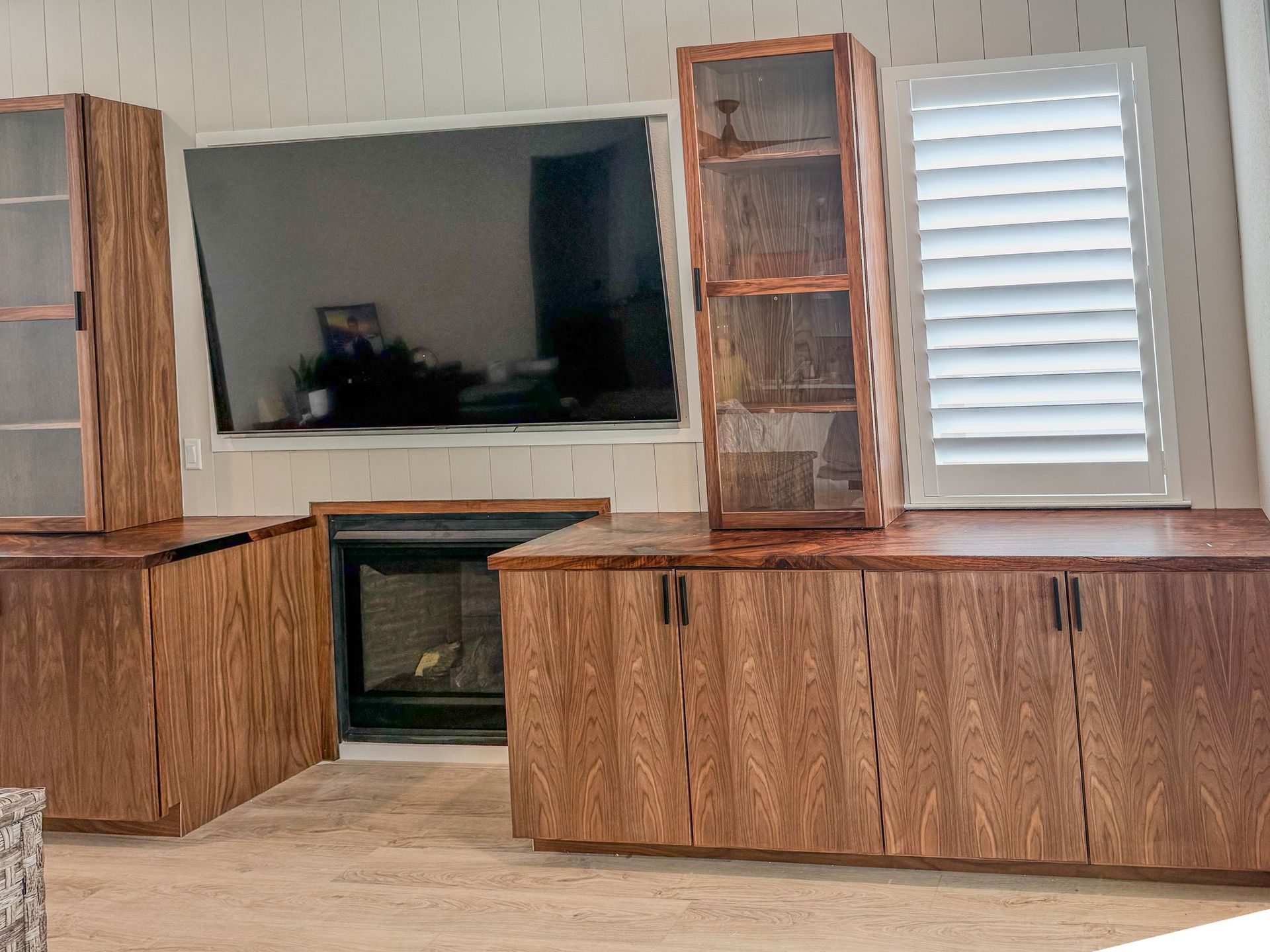 Wooden entertainment center with glass-front cabinets, fireplace, and window with shutters.