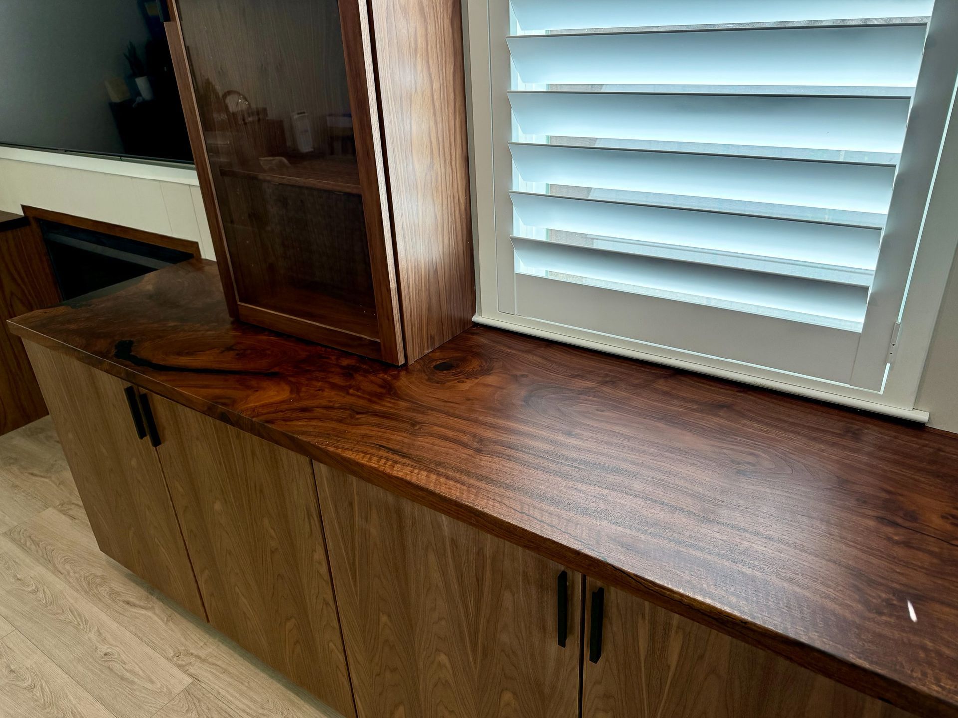Wooden cabinets and countertop with dark finish next to window with white shutters.