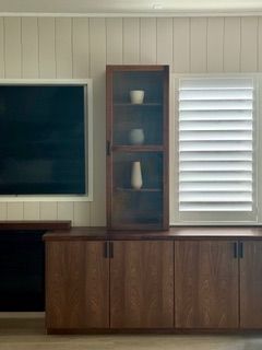Living room wall with TV, built-in cabinet, and white shuttered window above a wood credenza