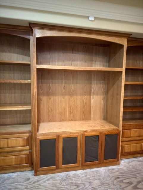 Built-in wooden bookshelves with a central alcove and lower cabinets in an empty room