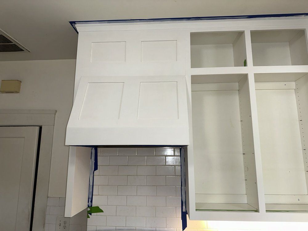 A kitchen with white cabinets and a hood