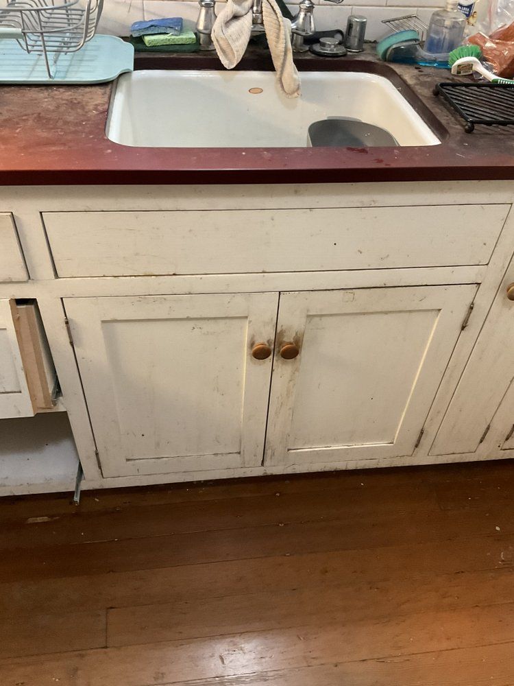 A kitchen sink with a wooden counter top and white cabinets.