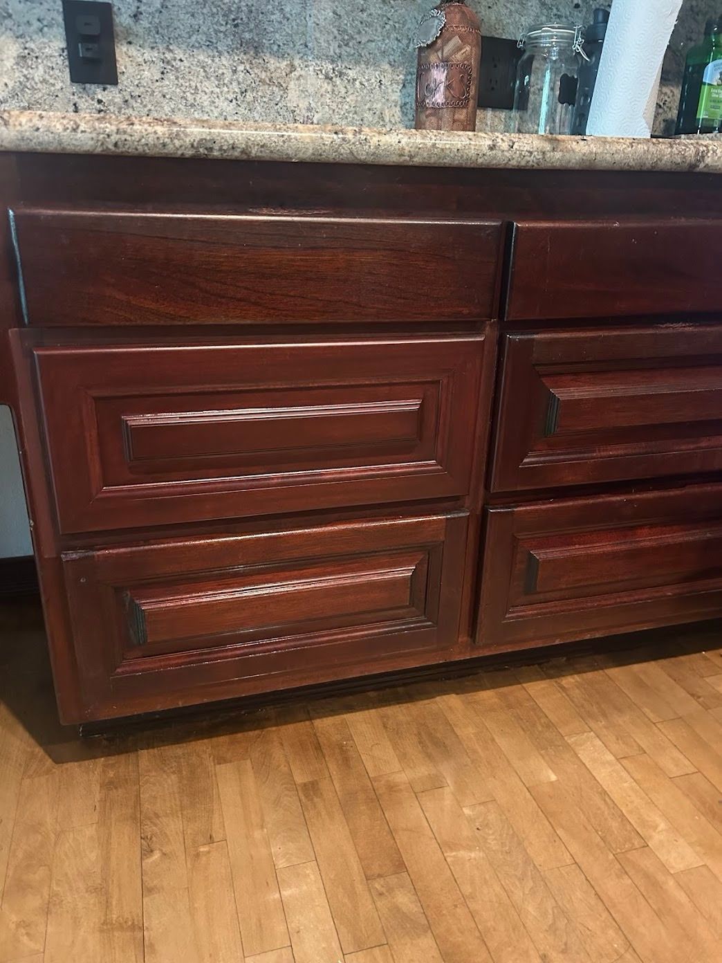 Dark mahogany kitchen cabinets with granite countertop above and hardwood floor below.