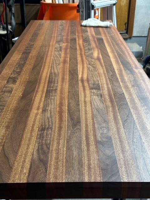 Close-up of a rectangular solid wood butcher block countertop with alternating dark and light wood grain strips.
