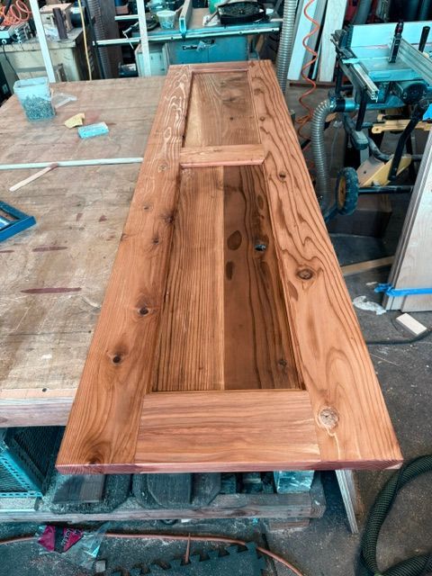 Finished solid redwood door on a workbench, stained brown with visible wood grain. The door has panel detailing.