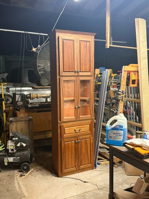 Tall wooden storage cabinet in a workshop with tools and equipment. It has upper and lower cabinets.