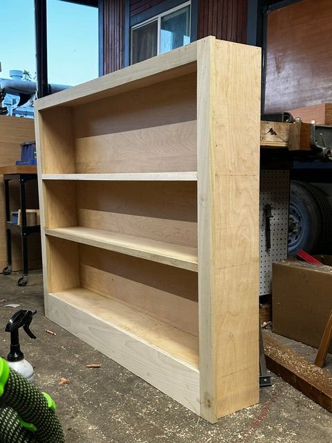 Wooden bookshelf with three shelves, sitting on a wooden floor. The bookshelf is light-colored.