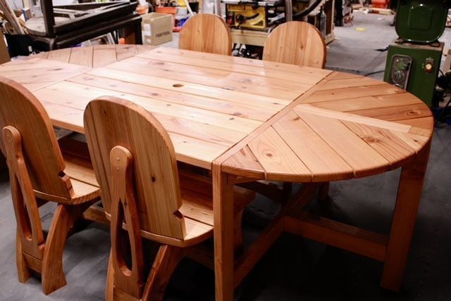 Redwood outdoor oval dining table with four matching chairs in a workshop setting. Table has extending leaves.