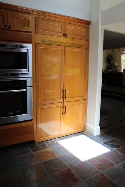 Built-in wood cabinets with a microwave, oven, and refrigerator in a kitchen with tile flooring.