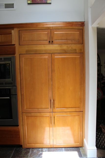 Built-in, light wood-tone cabinet with four custom refrigerator door panels and two upper cabinets in a kitchen.