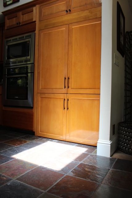 A kitchen with light wood refrigerator panels, including a microwave and oven. .