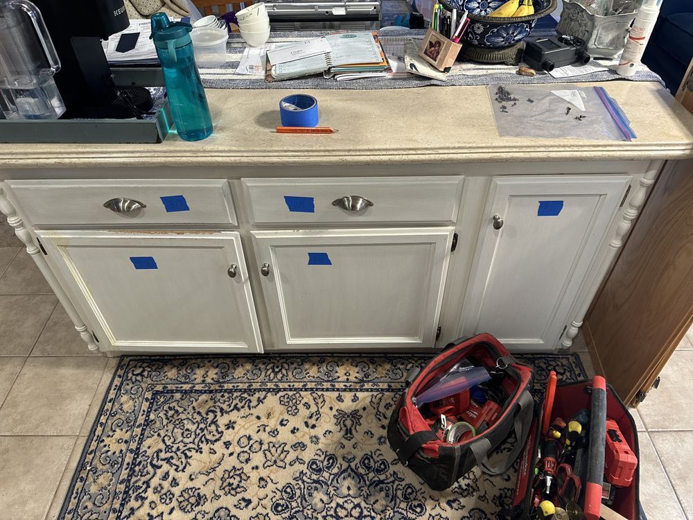 A kitchen counter with blue tape on it and a tool bag on the floor.