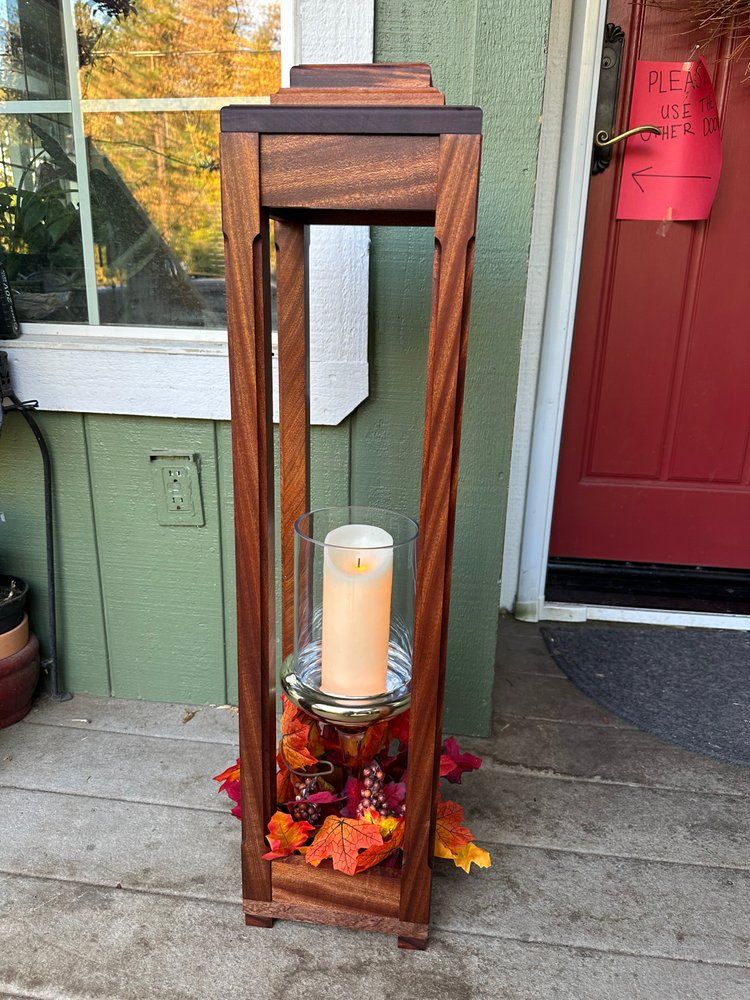 A wooden lantern with a candle in it is sitting on a porch.