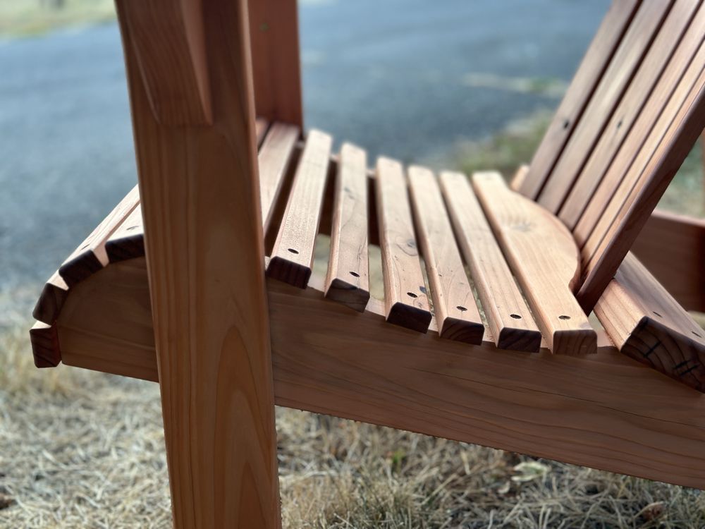 A wooden chair is sitting in the grass next to a road.