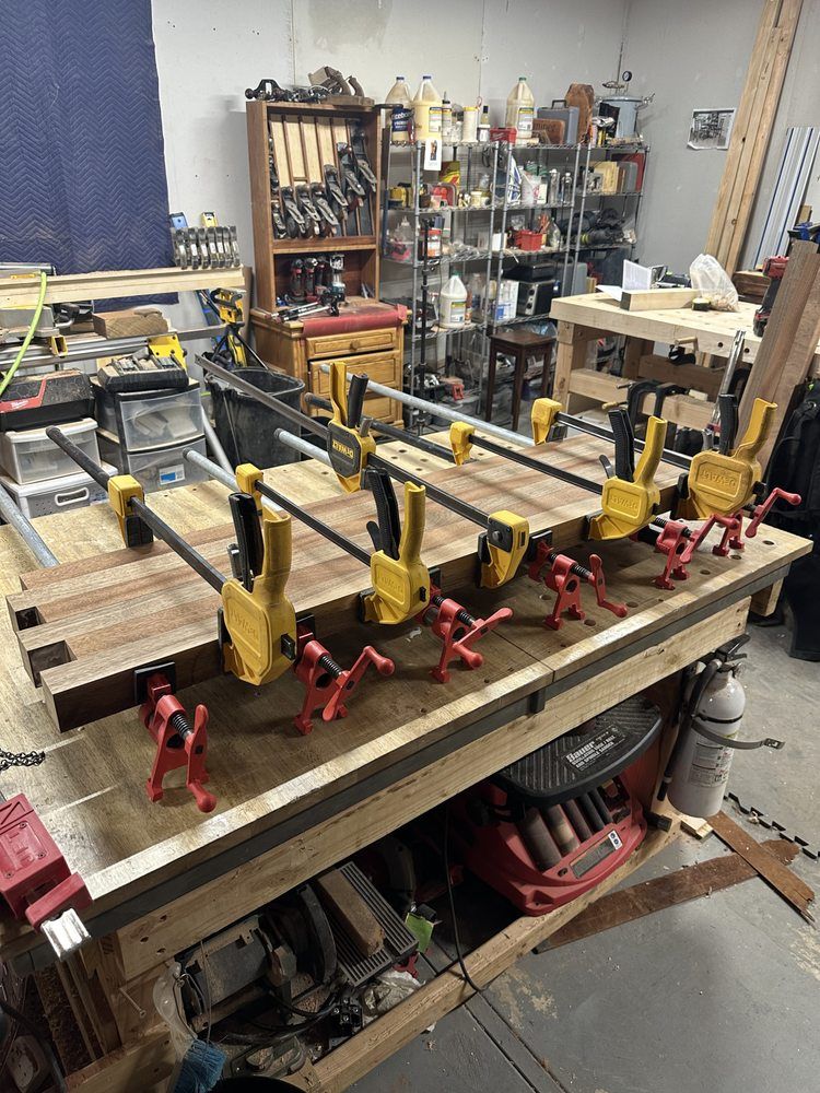 A bunch of clamps are sitting on top of a wooden table in a workshop.