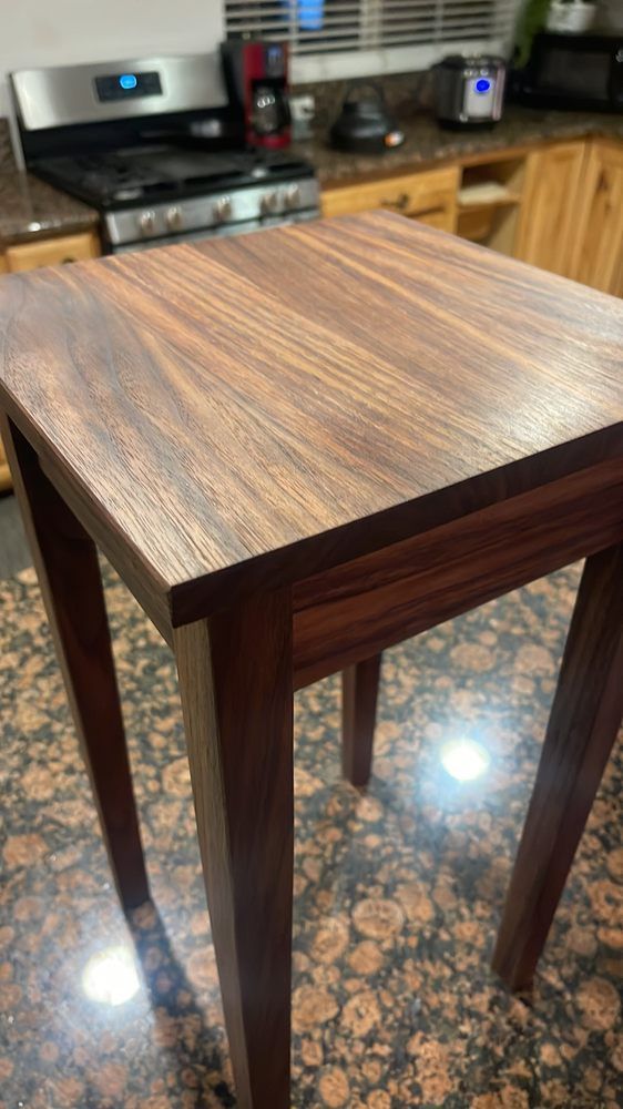 A small wooden table is sitting on top of a granite counter in a kitchen.