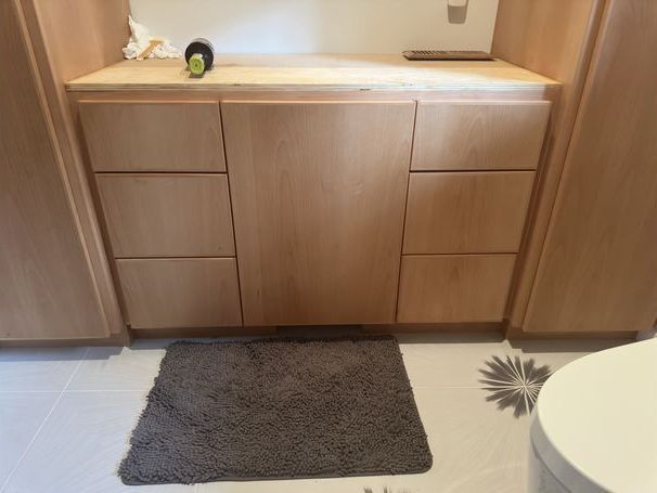 A bathroom with wooden cabinets , a toilet and a rug on the floor.