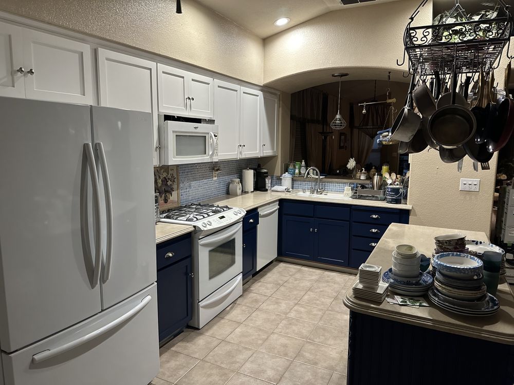 A kitchen with white cabinets and blue cabinets and a white refrigerator