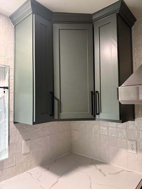 Kitchen corner with dark green cabinets, white tile backsplash, and light marble countertop
