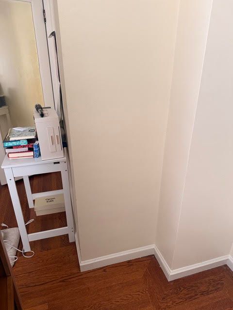 Narrow hallway corner with wood floor, white walls, and a small side table with stacked books.