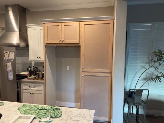Kitchen with unfinished wooden cabinet openings beside a stove and dining area.