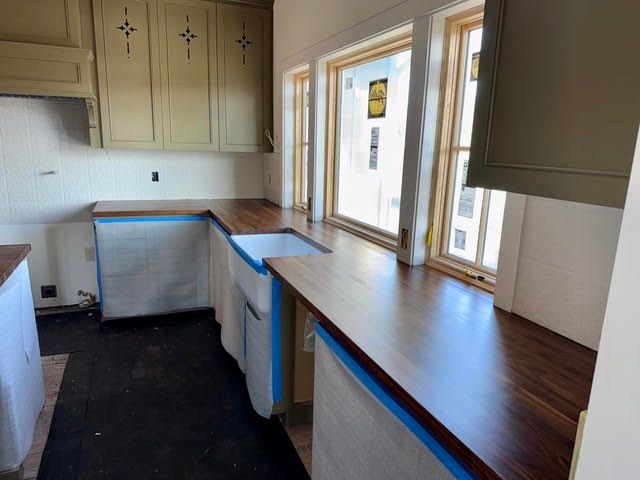 Empty kitchen with wooden countertops, cream cabinets, and a bright window over the sink.