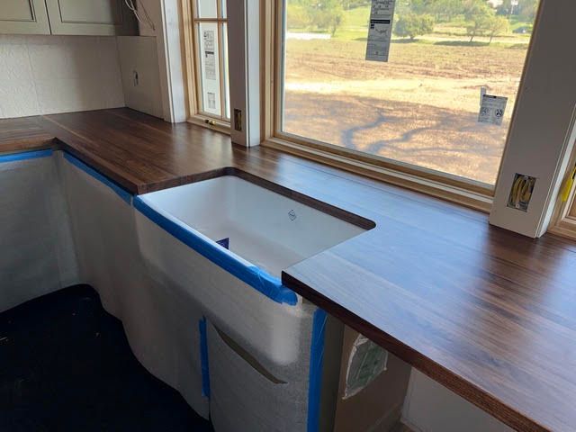 Kitchen counter under renovation with blue tape, white sink opening, and wood-look countertop by a window
