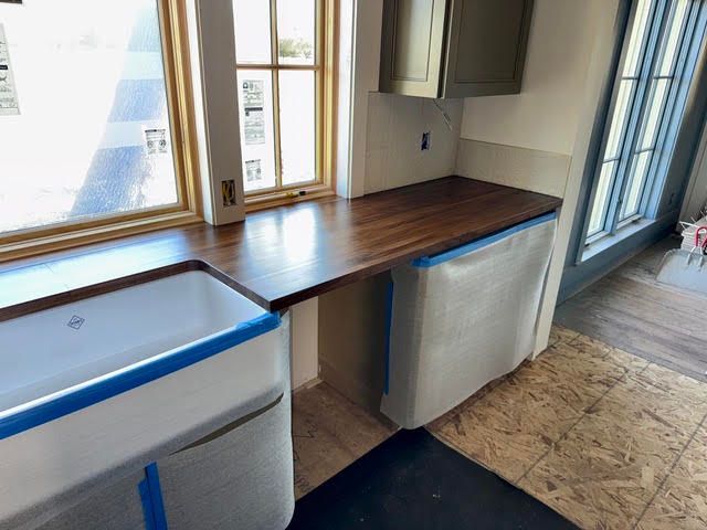 Kitchen with wood countertop, white cabinets, and two white appliances by a sunlit window