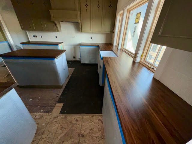 Narrow kitchen with cream cabinets, white appliances, and a long wood countertop by windows.