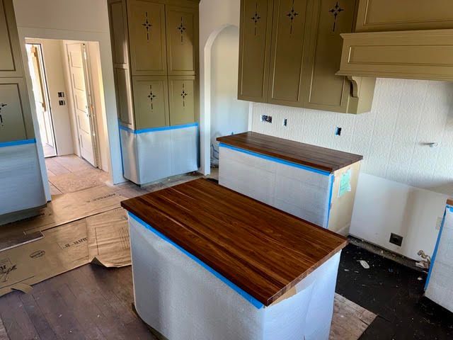 Kitchen under renovation with blue-taped cabinets, two wood-topped islands, and covered floors