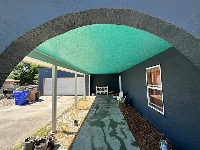 Covered walkway with turquoise ceiling, dark blue walls, and driveway leading to a garage.