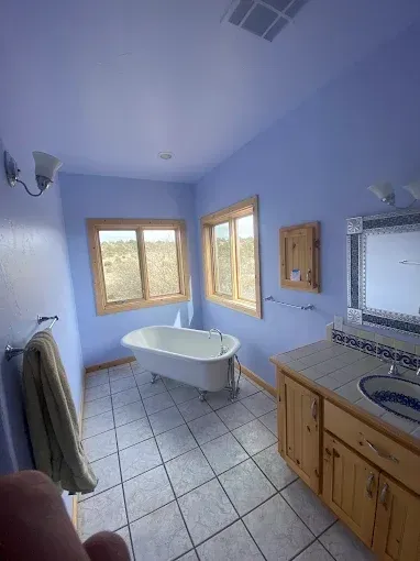 Bathroom with a clawfoot tub, blue walls, wooden cabinets, and tiled floor.