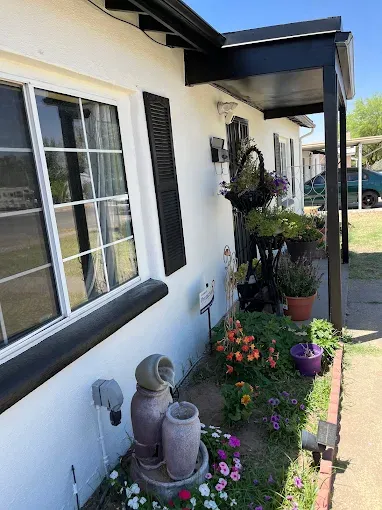 White house with flower garden and porch, black shutters, pots, and water fountain.