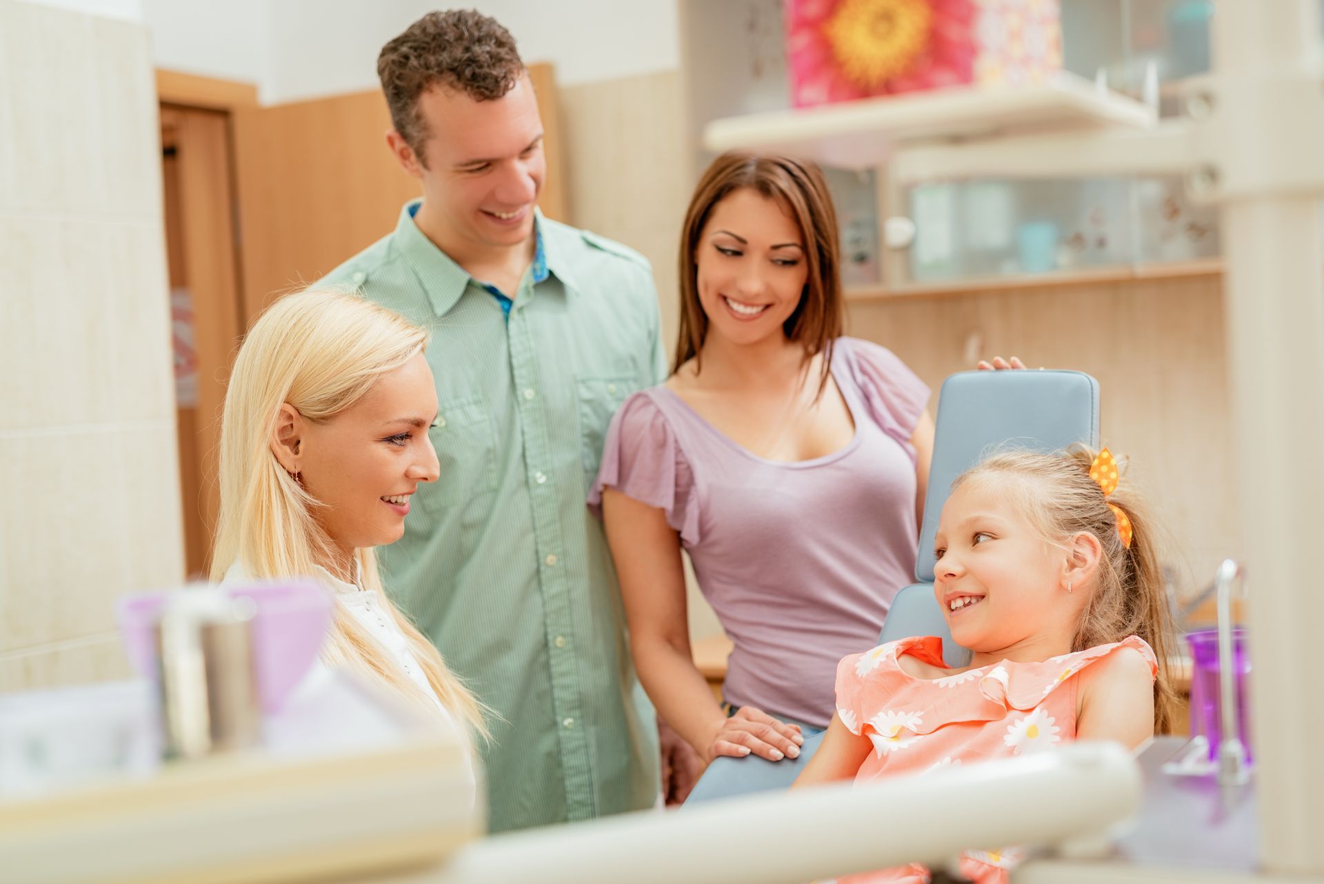 Dentist consults child in chair as parents observe supportive visit.
