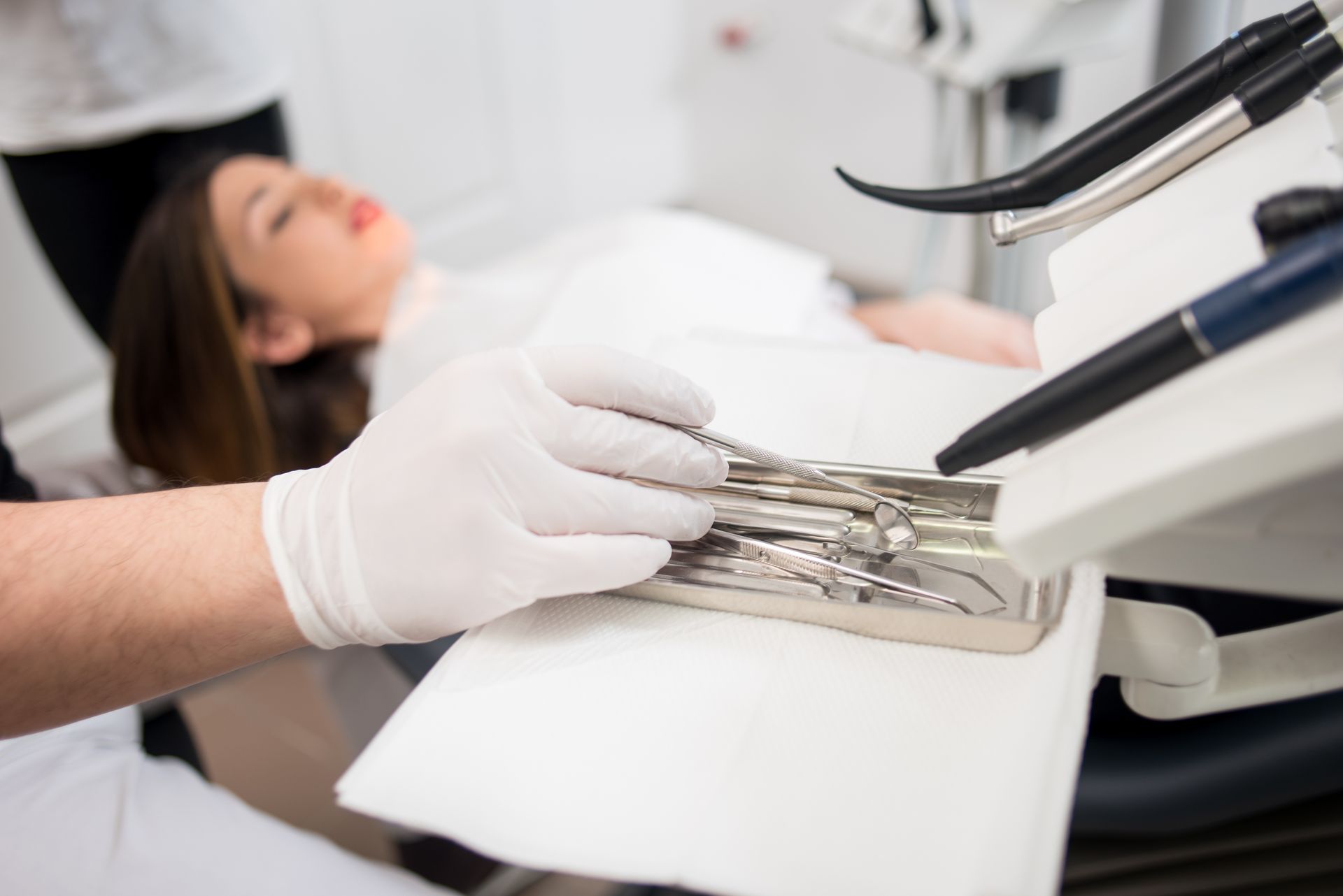 A dentist with gloved hands is treating a patient with dental tools in a dental clinic.