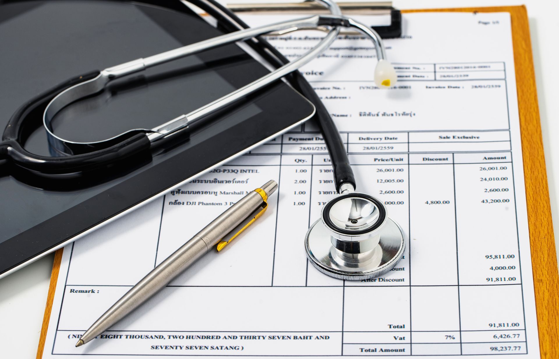 A stethoscope is sitting on top of a clipboard next to a pen and a tablet