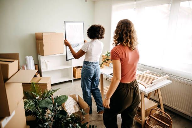 Two women are moving into a new home and hanging a picture on the wall.