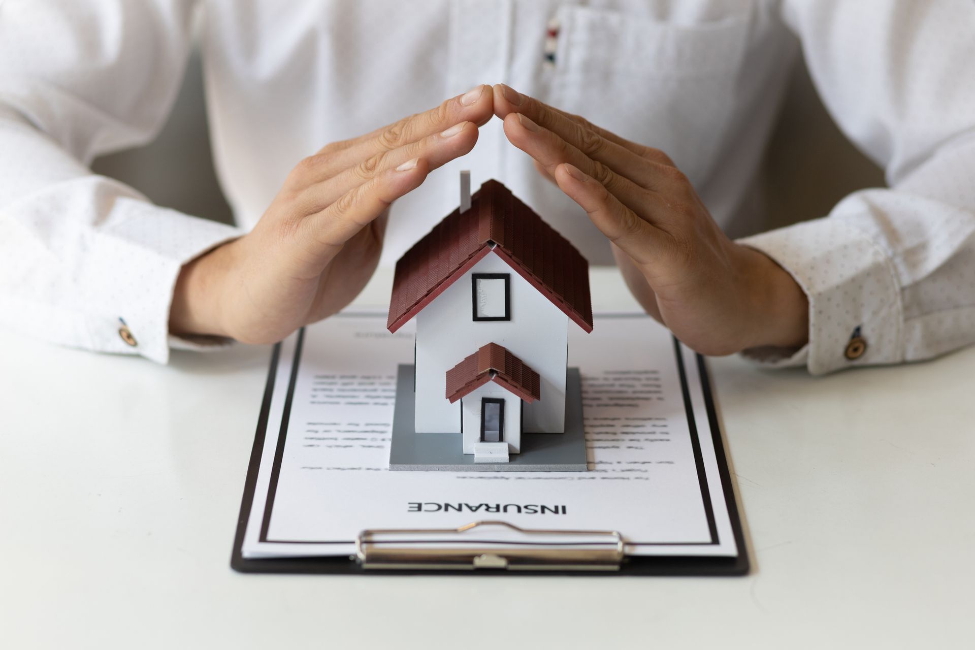 Cropped view of an insurance agent forming a home with their hands above a home insurance agreement.