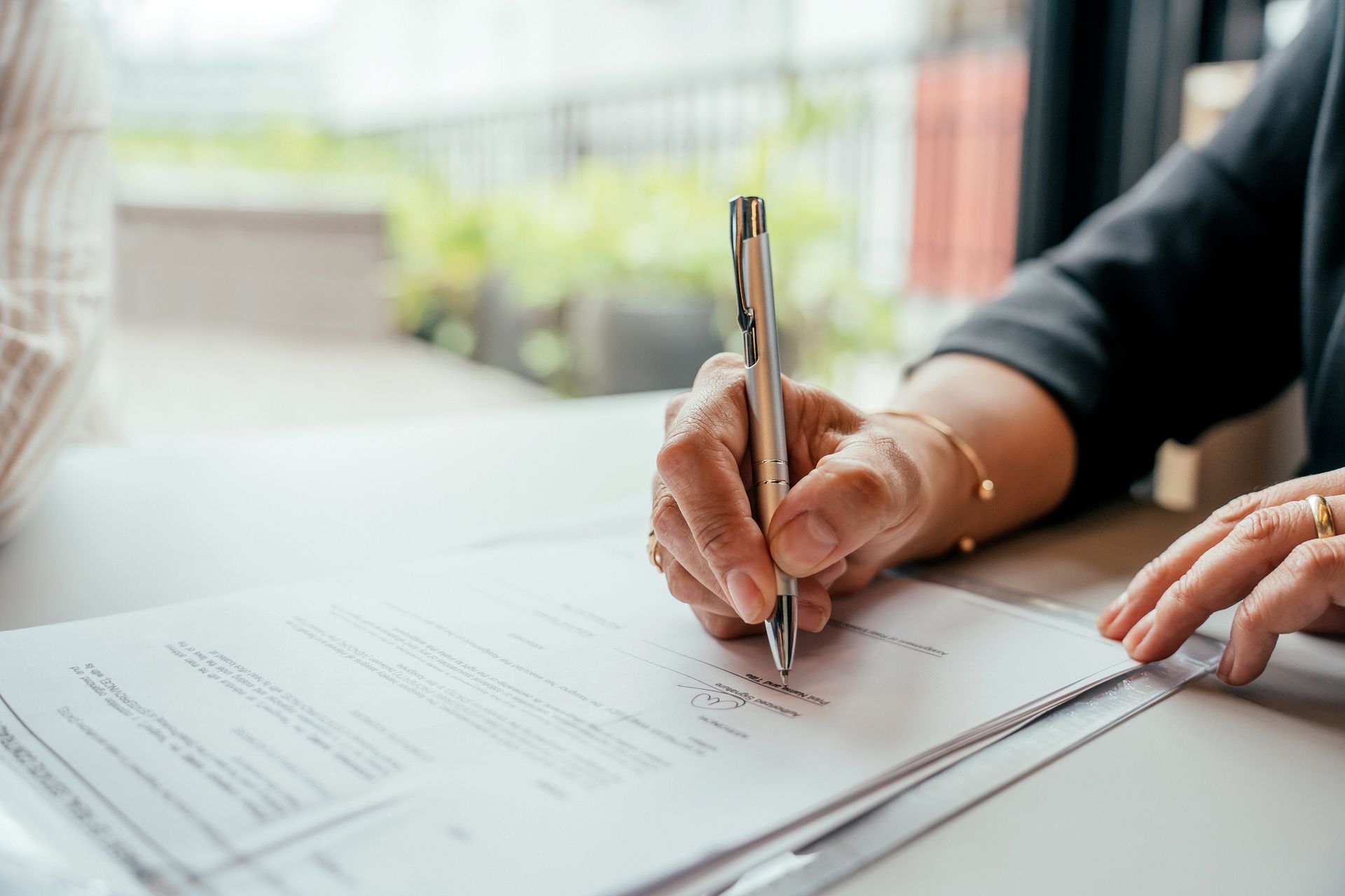 Close-up of a hand signing a document with a pen on a desk.