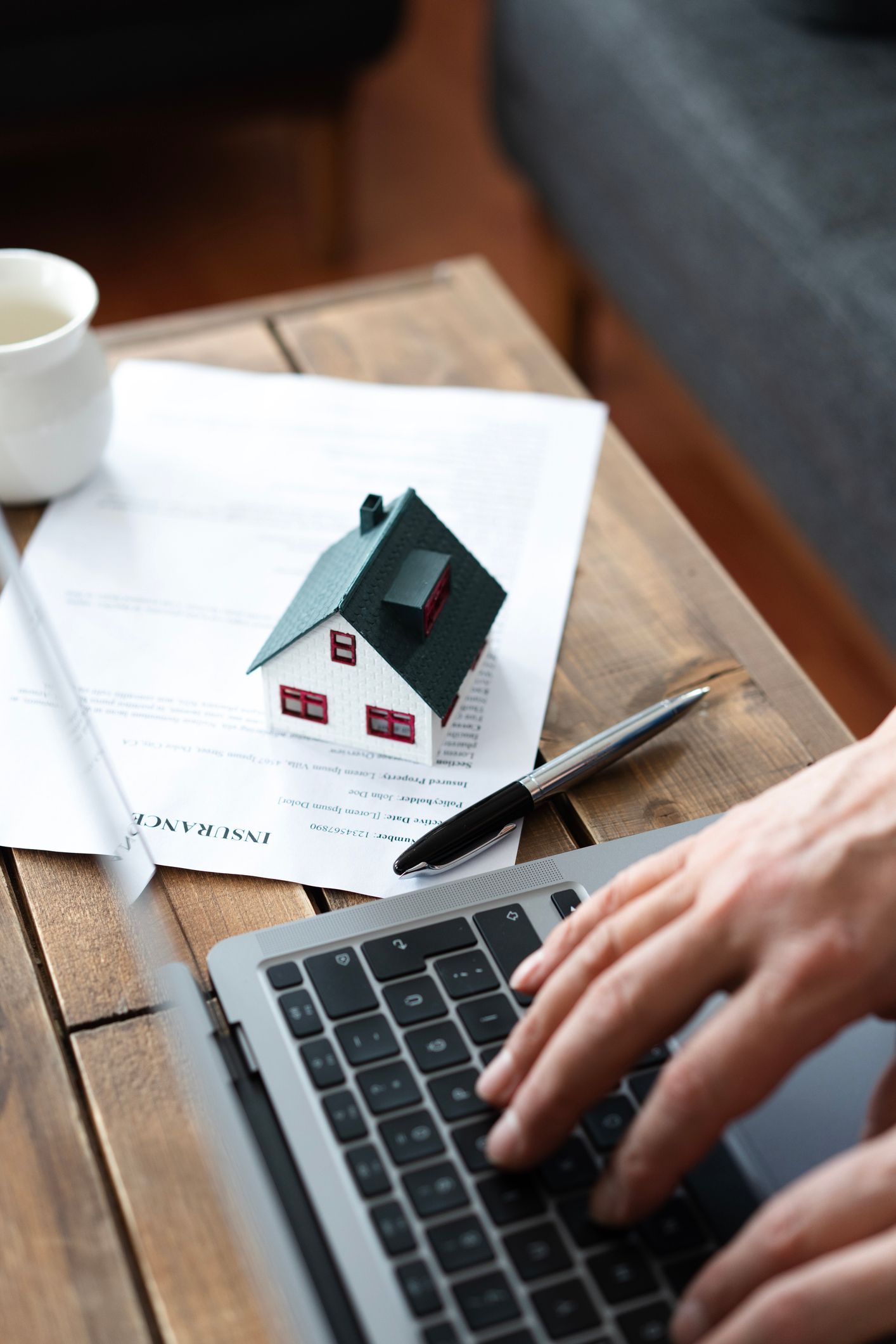 Insurance agent works on a laptop with home policy documents and house model on the desk. 
