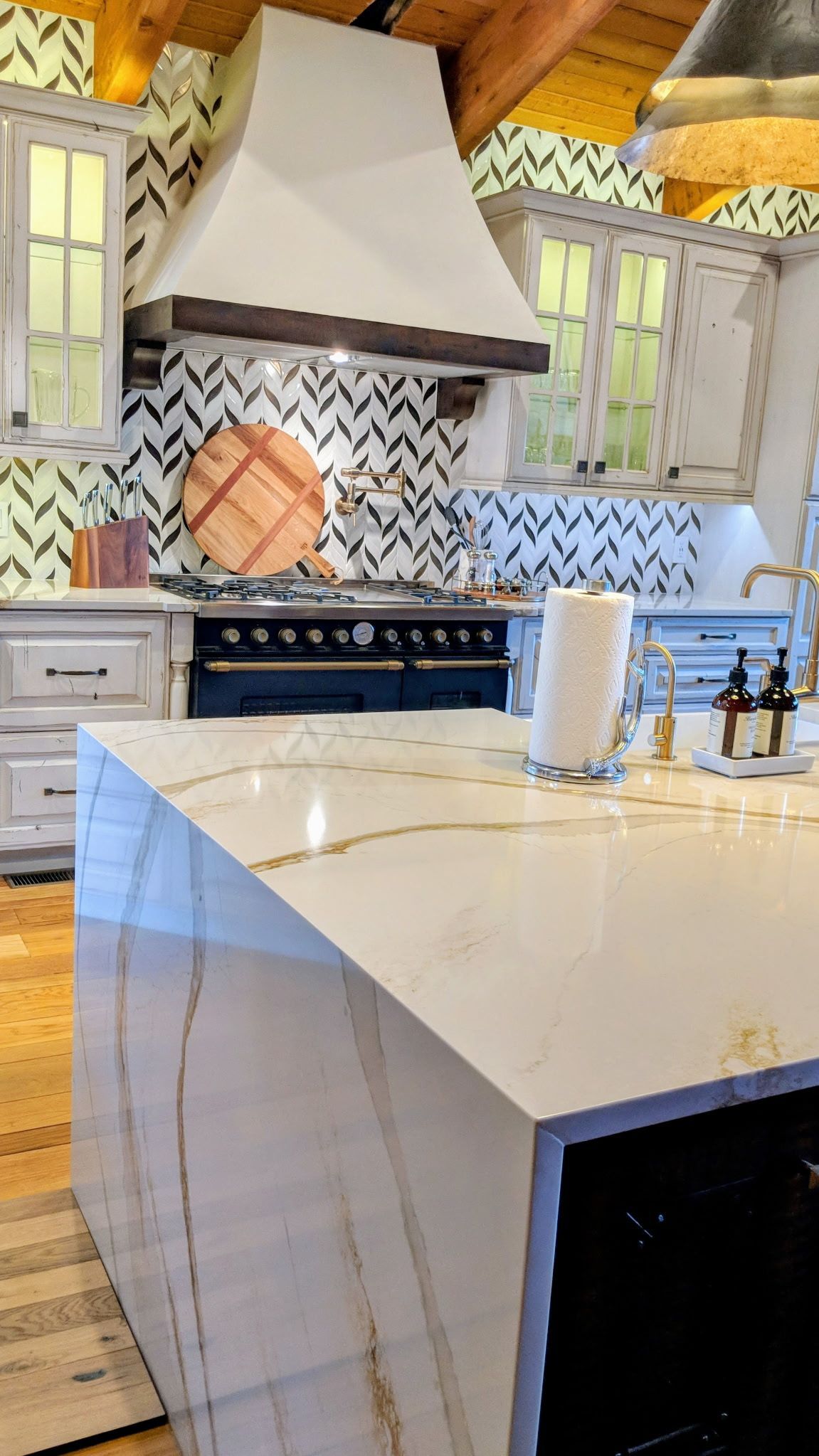 Kitchen with white quartz countertop, oven, and cabinetry. Chevron tile backsplash and range hood.