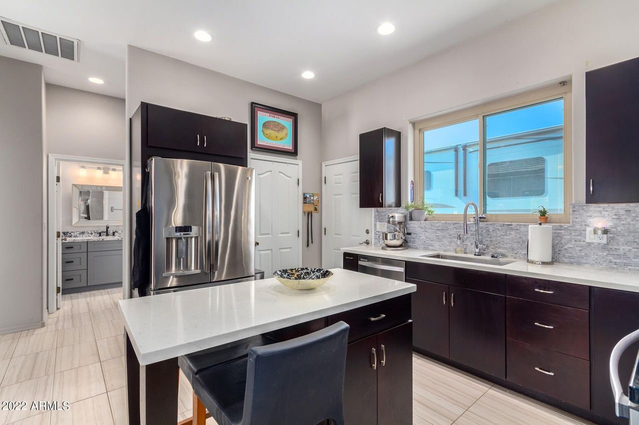 Kitchen with dark cabinets, stainless steel fridge, and white countertops; a bathroom visible in the background.