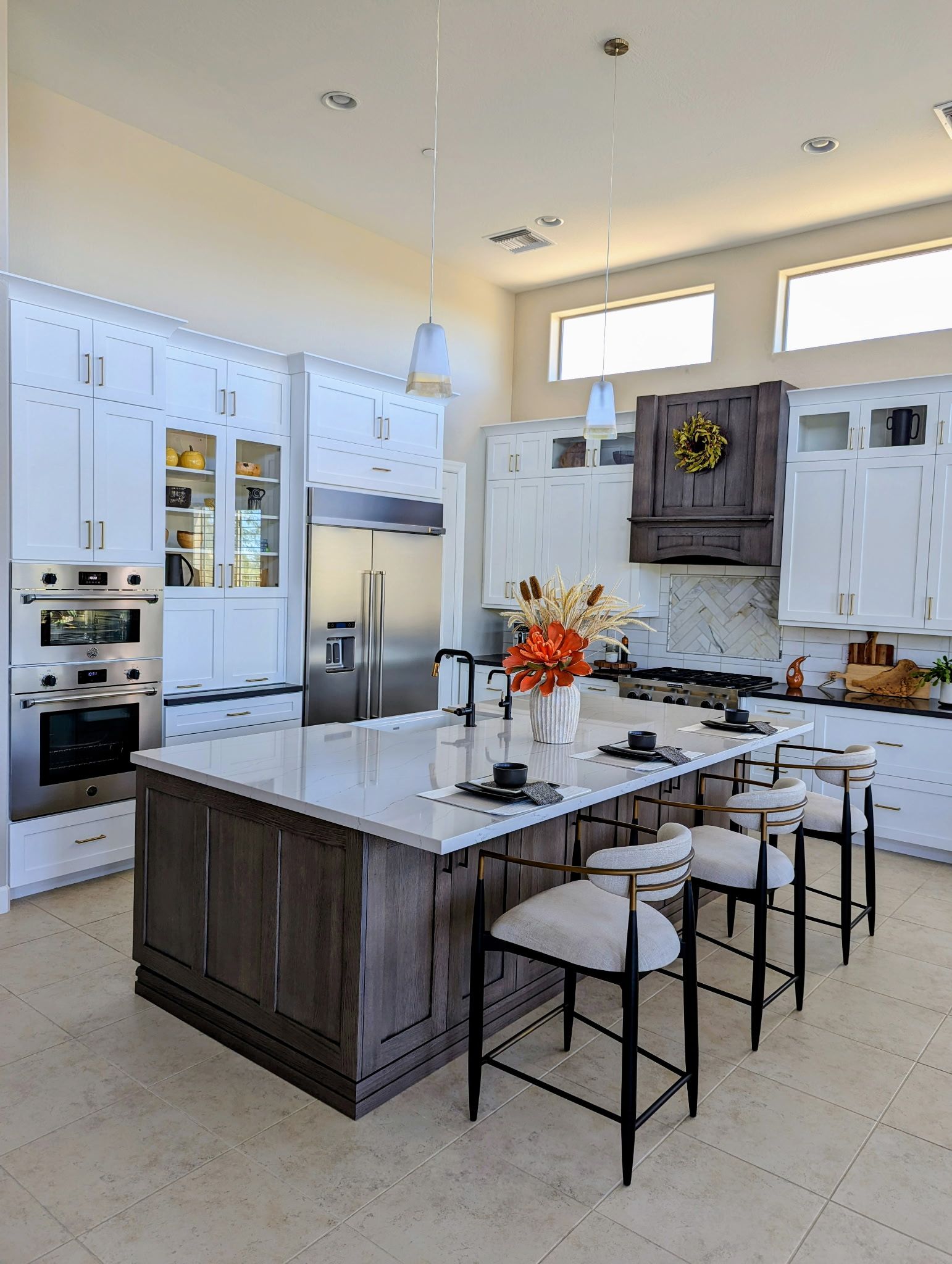 Modern kitchen with white cabinetry, dark island, and seating. Stainless steel appliances and natural light.