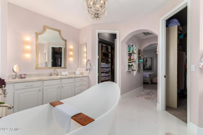Elegant, pale pink bathroom with a white tub, double vanity, and walk-in closet.
