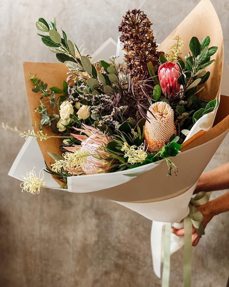 A Person is Holding a Bouquet of Flowers Wrapped in Brown Paper — Suncoast Flowers in Buderim, QLD