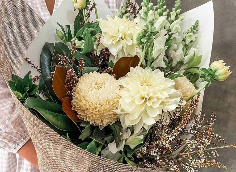 Neutral-toned bouquet with cream flowers and greenery wrapped in paper.